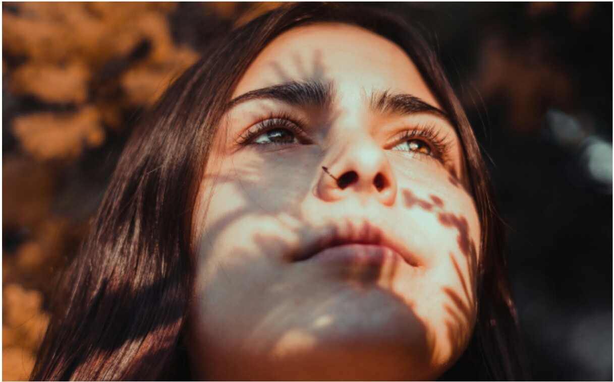 A woman looking up with dappled sunlight on her face